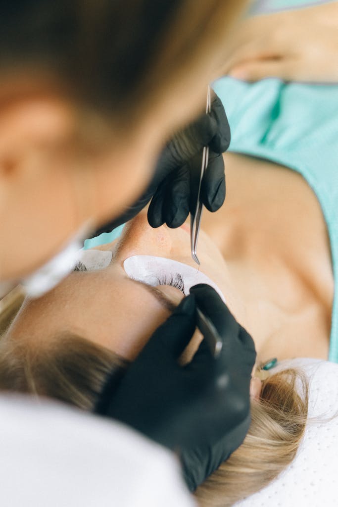 A beautician applies eyelash extensions to a client's lashes in a beauty salon.